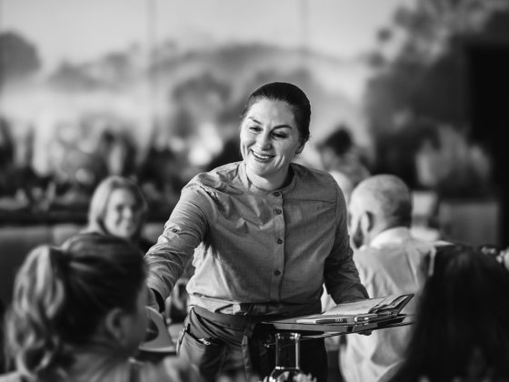 a restaurant server reaching to deliver a drink to a table of diners