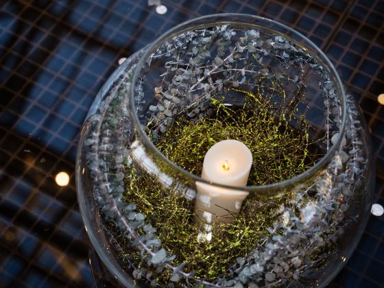 Closeup of a glass sphere containing a white glowing candle nestled in greens and dried plant material.