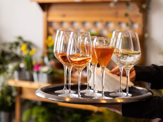 Closeup of server holding a tray of wine glasses, with wood and floral accents in the background.