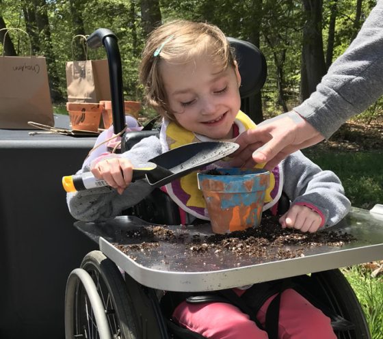 child in wheelchair uses shovel to place soil in hand-painted flowerpot