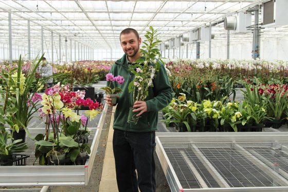 Greg Griffis smiling for the camera and holding orchids in his hands 