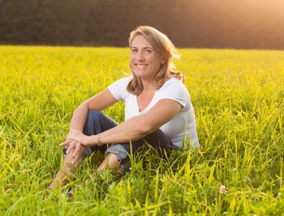 image of person sitting in a field of grass with trees and the sun behind
