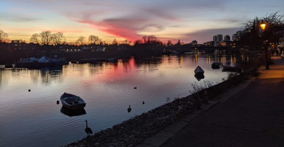 A sunset image over a river with small boats and geese wading.