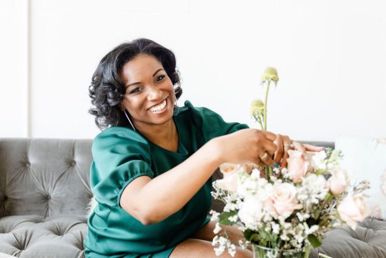A person in an emerald shirt sitting on a gray sofa creating a floral arrangement.