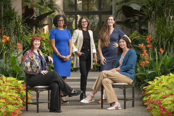 A group of 5 people, some sitting, some standing, in a garden setting.
