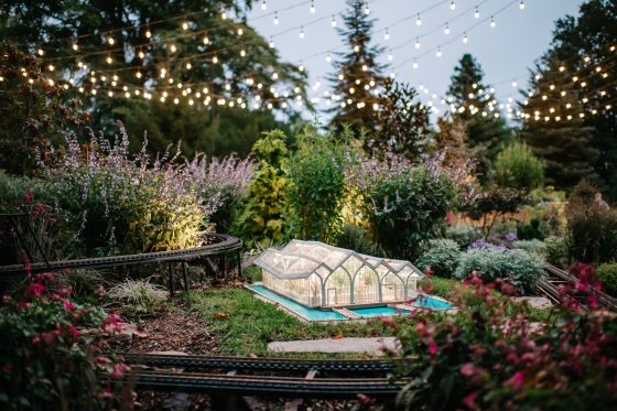 A model of a glass conservatory sitting in an outdoor model train display.