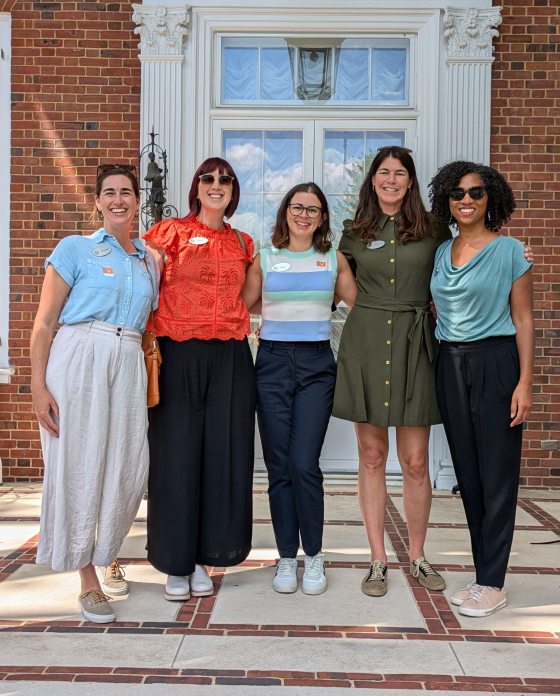 Five people standing shoulder to shoulder in front of a brick building, posing for the camera.