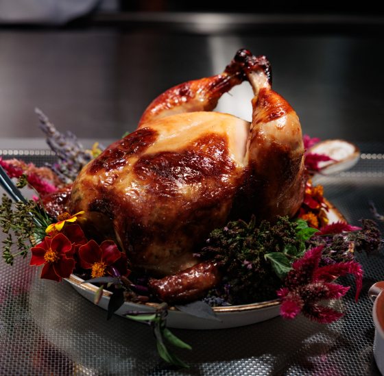 A person plating a whole roasted chicken on top of a bed of flowers. 