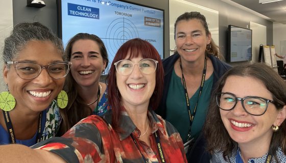A selfie of 5 adults with a classroom in the background. 