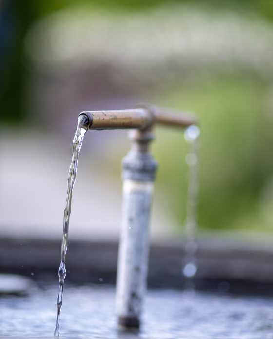 A t-shaped water fountain, with water coming our of both ends of the "t" into a pot. 