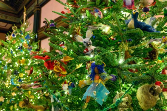 A vertical shot of a heavily decorated Christmas tree. The ornaments are unique, including a central needle-felted white rabbit with a red scarf, a figure with a blue fabric skirt, a felted blue bird, and various other whimsical animal ornaments.