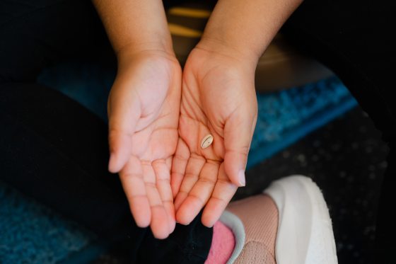 A pair of cupped hands holding a single, small, light-colored seed, shown from a top-down perspective during a children's activity.