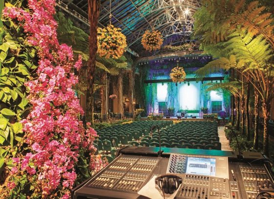 sound equipment nestled between flowers with a view of stage and rows of seats 