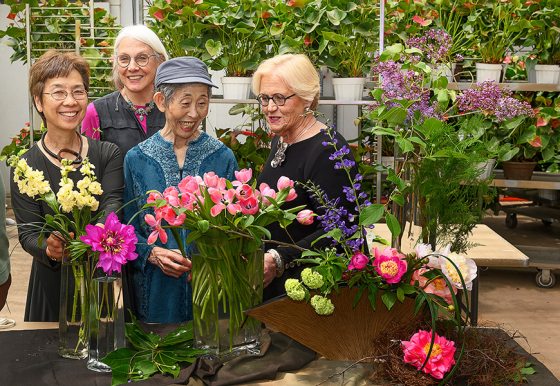 Four floral designers smile broadly at the floral creations in front of them.