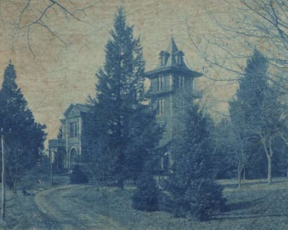 a scanned photograph of a large victorian home surrounded by evergreen trees