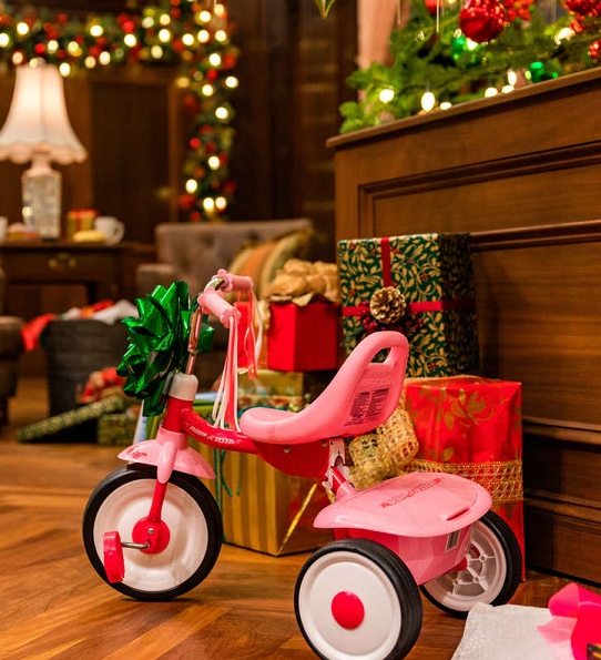 a pink tricycle with a green bowl on it and wrapped presents in the background 