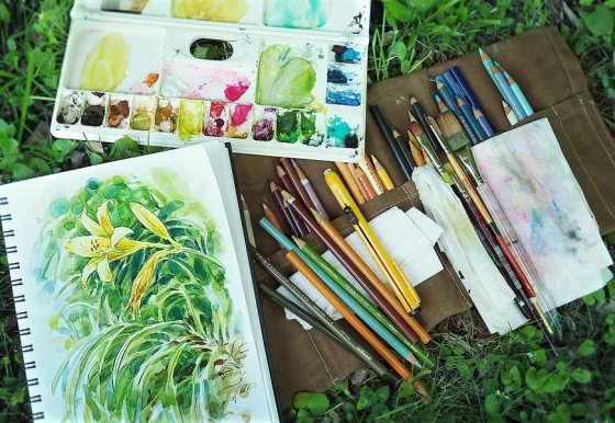 a canvas of a painted yellow lily and paint supplies placed on a patch of grass