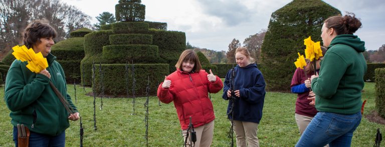 two students smile at the camera with one putting thumbs up in front of the topiary garden