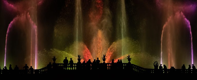 silhouetted figures stand in front of towering jets of illuminated water