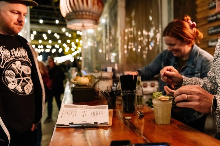 a bartender serves botanically-inspired cocktails to two people at an outdoor bar