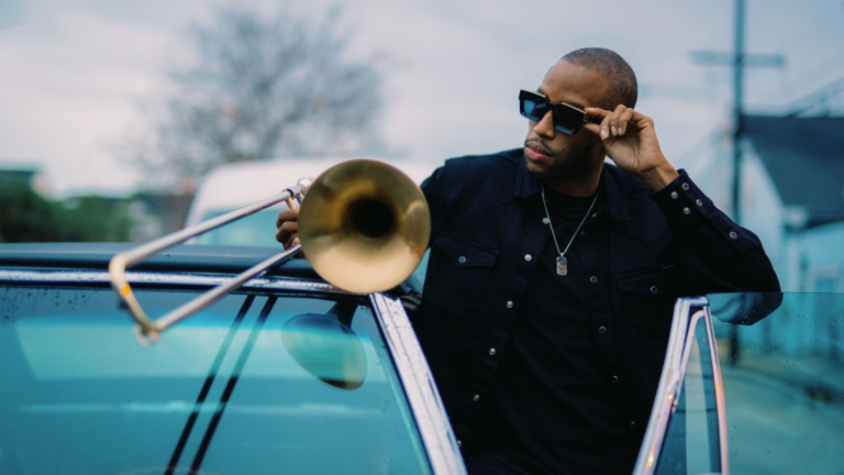 trombone shorty standing next to a car with the door open holding a trombone