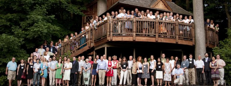 large group of alumni pose in front of a treehouse