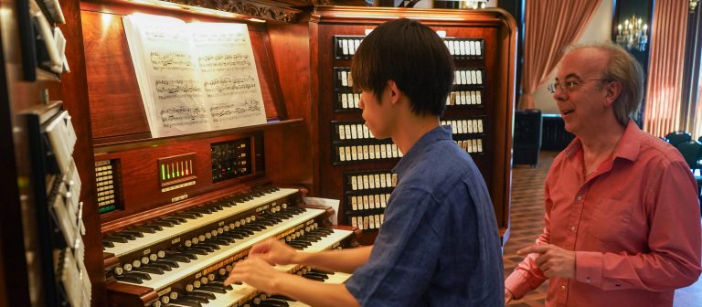 an instructor stands next to a student at the organ console