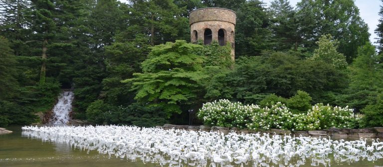 a stone tower in the background with plastic white flamingoes wading in a pond below it