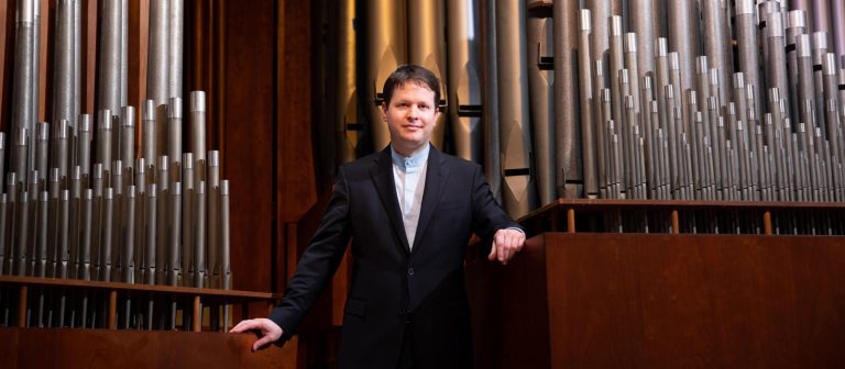 Adult standing in front of organ pipes.