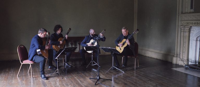 Four adults seated playing the guitar.