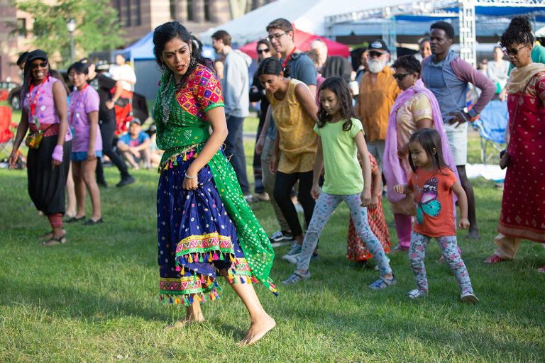 A person in traditional Indian dress leads a multi-generational group in dance