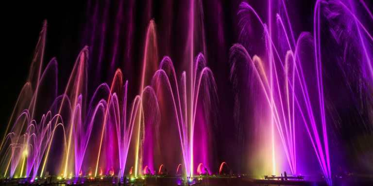 tall fountains lit in yellow, fuchsia, and purple against a dark night sky