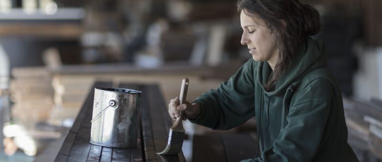 a person in a dark green sweatshirt applies a paintbrush to a dark wood surface