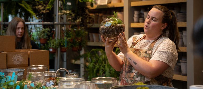 a person surrounded by plant containers holding a terrarium in their hands