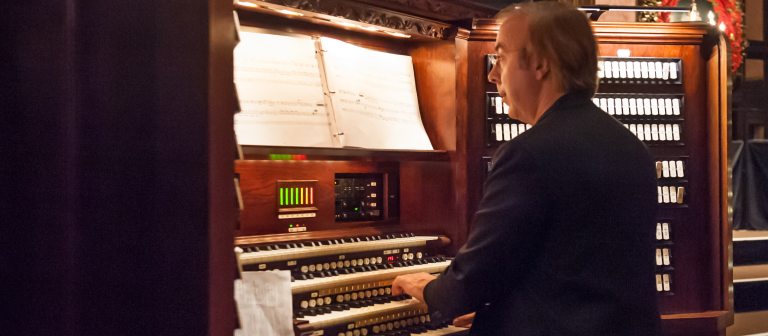 a person seated at an organ console, hands on the keys