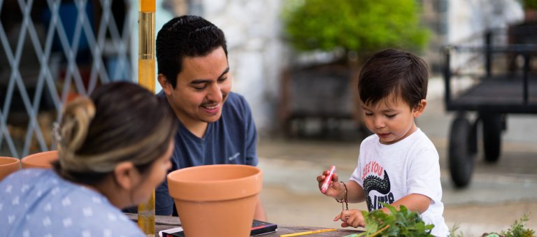 Parents help a young boy decorate a terra cotta pot