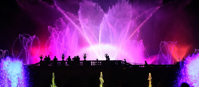 Fountains lit up at night in pink and red lights. 