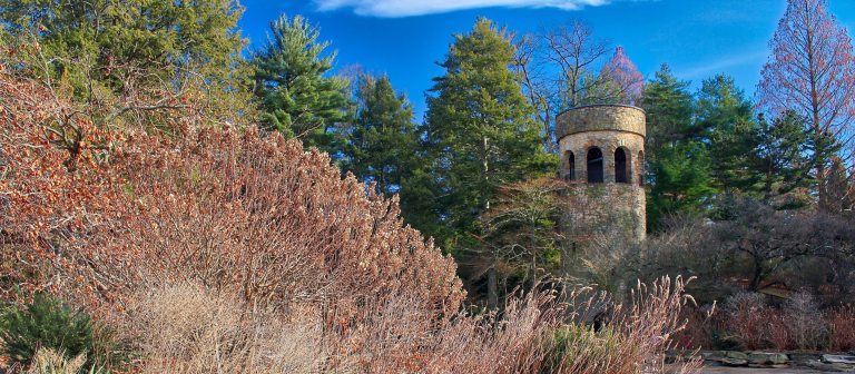 A landscape at Longwood Gardens featuring a stone tower and hillside plantings.