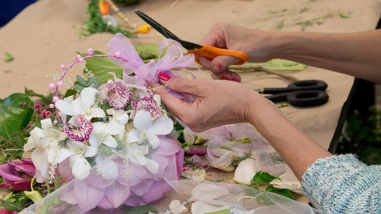 A person's hands holding scissors while creating a floral arrangement.
