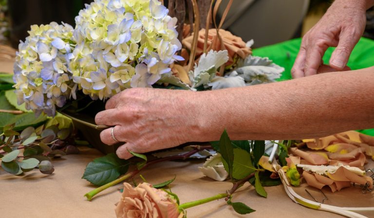 A person creating a floral arrangment out of white and purple hydrangeas.