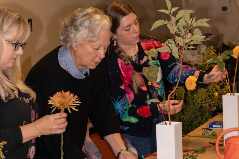 Three people standing at a table creating a floral design.