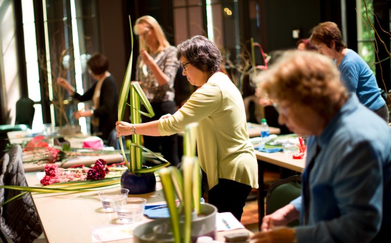 Several people standing at a table arranging floral greenery into vases.