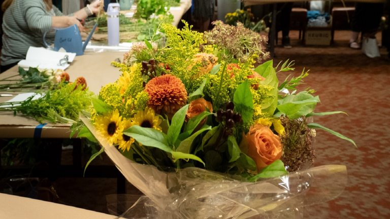 A bouquet of fall flowers in a black bucket on a table.