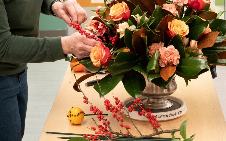 A person creating a floral arrangement filled with green foliage and peach colored flowers.