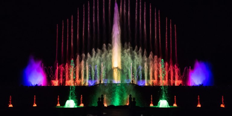 Water from fountains shoots into the air and is illuminated in many colors at night.