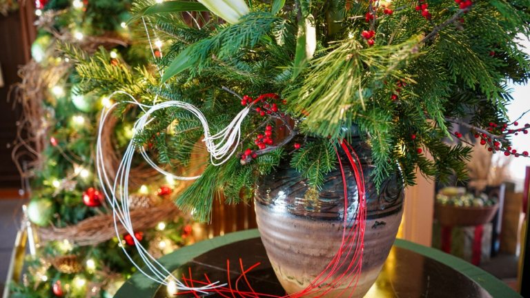 A vase filled with holiday greens and red ribbon resting on a glass table.