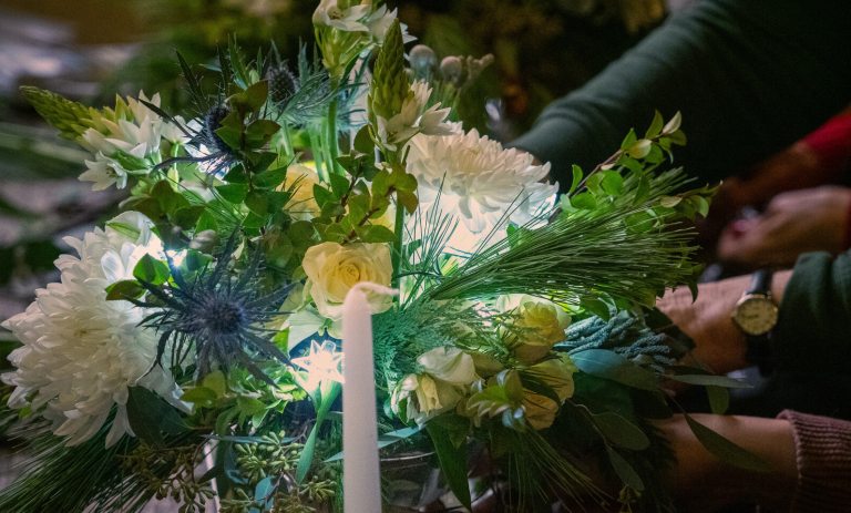 A holiday flower bouquet featuring white florals, white lights, and a candle in the center.