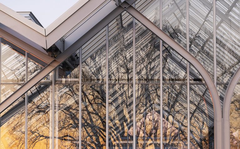The outside of a glass conservatory with the reflections of bare trees on the panes.