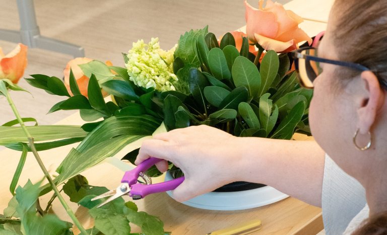 A person holding shears and creating a floral arrangement.