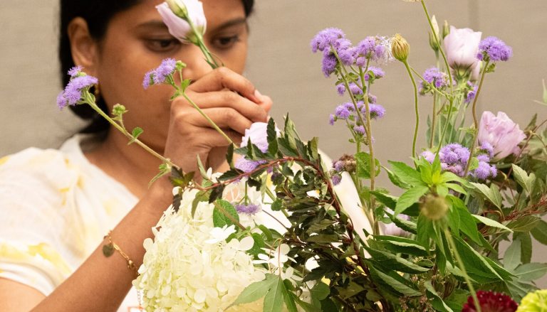 A person adding flowers to a floral arrangement they are creating.